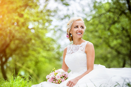 Beautiful young bride in wedding dress sitting in the grassの写真素材
