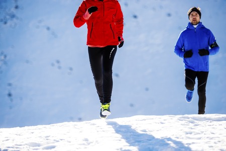 Young couple jogging outside in sunny winter mountains