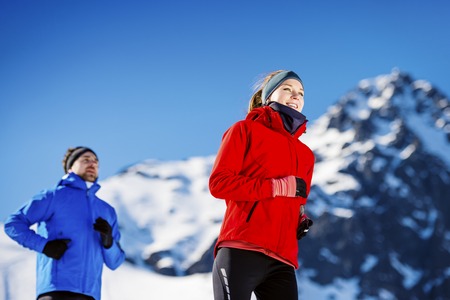 Young couple jogging outside in sunny winter mountainsの写真素材