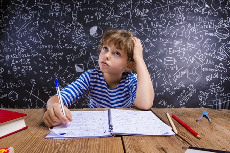 Cute little girl doing her homework in front of big blackboard