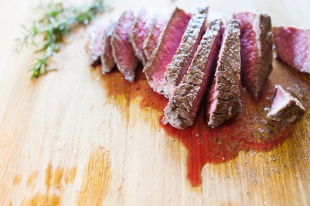 Grilled beef steak, sliced, on a wooden cutting board with fresh rosemary springの写真素材