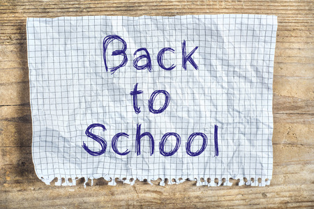 Piece of old rumpled paper with Back to school sign on wooden floor backgroundの写真素材