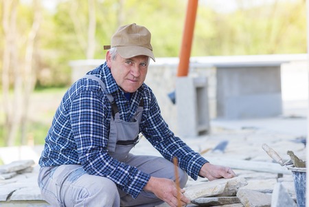Senior man  in checked shirt laying a stone pathの写真素材