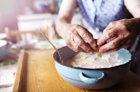 Senior woman baking pies in her home kitchen.  Adding egg.の写真素材