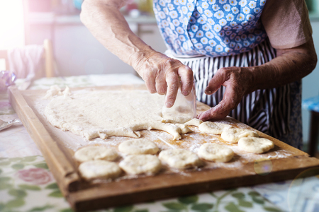 Senior woman baking pies in her home kitchen. Cutting out circles from raw dough.の写真素材