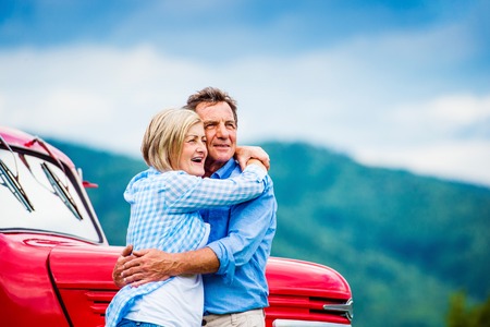 Senior couple standing by their vintage red carの写真素材