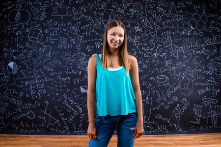Beautiful young school girl with notebook in front of big blackboardの写真素材