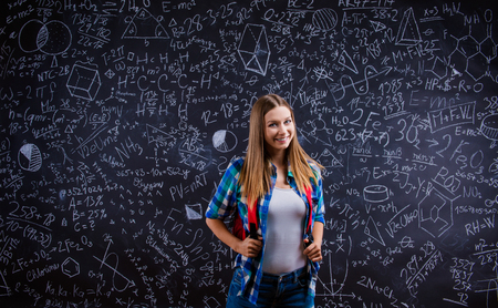 Beautiful young school girl in front of big blackboard. Studio shot on black background.