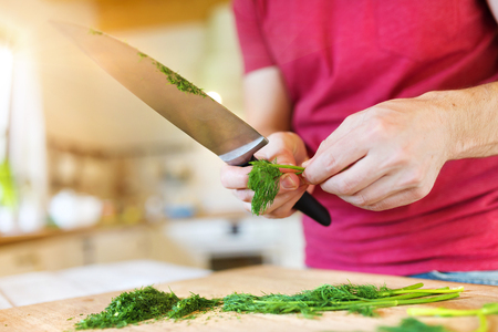 Young man cutting dill in his domestic kitchenの写真素材