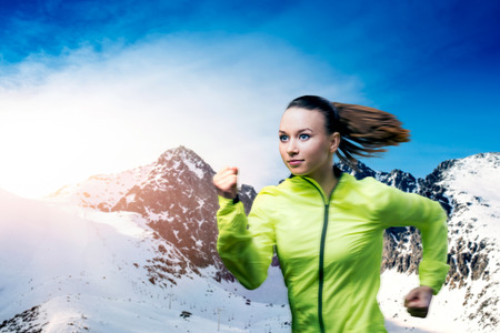 Young woman jogging outside in sunny winter mountainsの写真素材