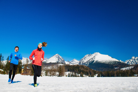 Young couple jogging outside in sunny winter mountainsの写真素材