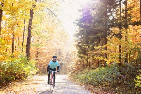Young handsome sportsman riding his bicycle outside in sunny autumn natureの写真素材