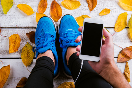 Unrecognizable runner with smart phone. Studio shot on wooden background.