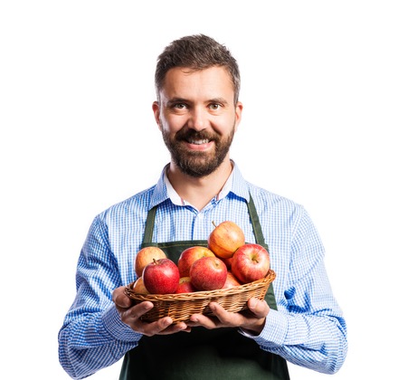 Young handsome gardener holding a basket full of apples. Studio shot on white backgroundの写真素材