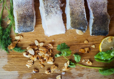 Raw zander fish fillets with roasted almonds and herbs on a wooden cutting board.の写真素材