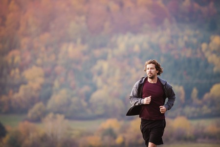 Young handsome runner outside in sunny autumn natureの写真素材