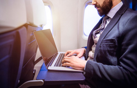 Unrecognizable young businessman with notebook sitting inside an airplaneの写真素材