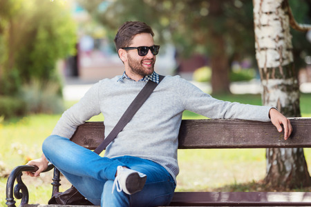 Handsome young man sitting on park benchの写真素材