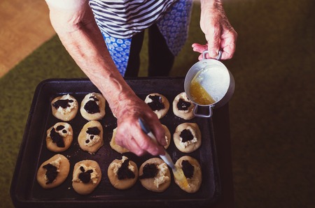 Senior woman baking pies in her home kitchen.  Brushing the buns with melted butter.の写真素材