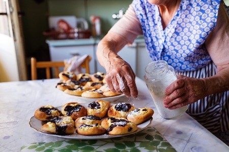 Senior woman baking pies in her home kitchen. Sprinkling freshly baked buns with powdered sugar.の写真素材