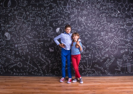 Cute little boy and girl in front of a big blackboard. Studio shot on black background.の写真素材
