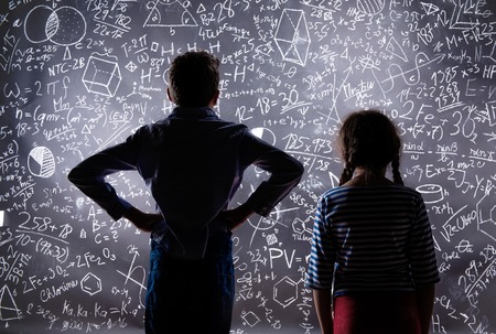 Cute little boy and girl in front of a big blackboard. Studio shot on black background.の写真素材