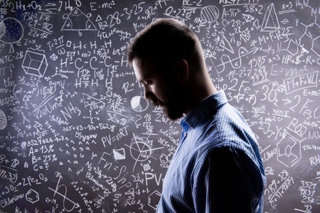 Teacher silhouette against big blackboard with mathematical symbols and formulas. Studio shot on black background.の写真素材