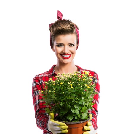 Woman in red checked shirt with pin-up make-up and hairstyle holding flower pot with yellow daisies. Studio shot on white backgroundの写真素材