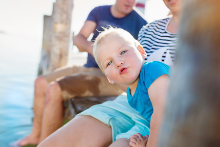 Cute little boy with his parents sitting on the pier on sunny summer dayの写真素材