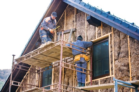 Construction workers standing on scaffold thermally insulating house facade with glass wool.の写真素材