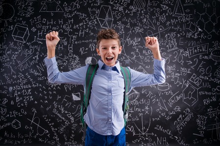 Excited and victorious boy against big blackboard with mathematical symbols and formulasの写真素材