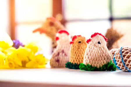 Colorful crocheted Easter chickens and fresh daffodil bouquet laid on white wooden tableの写真素材