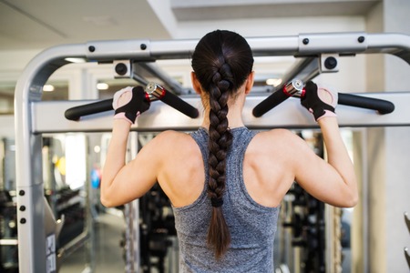Close up of attractive fit woman flexing back muscles on cable machine, back view, rear viewpoint
