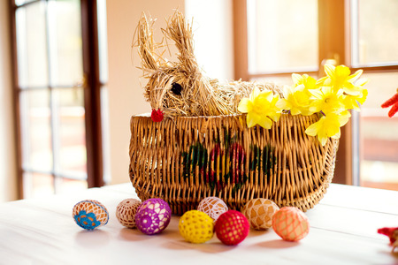 Wicker basket with straw Easter bunny and daffodils, crocheted eggs laid on wooden tableの写真素材
