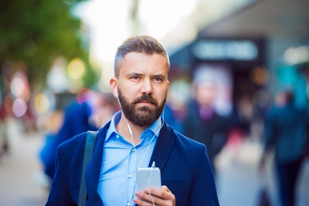 Hipster manager holding a smartphone listening music outside in the streetの写真素材