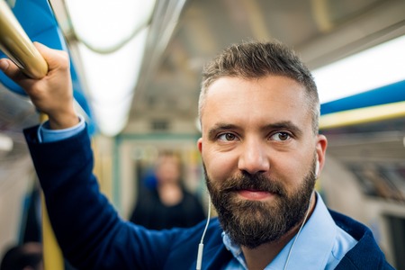 Close up of face of businessman with headphones travelling to work. Standing inside underground wagon, holding handhandle.の写真素材