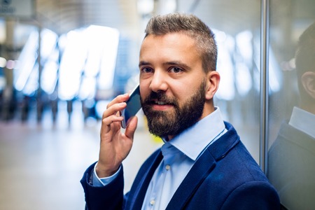 Close up of hipster businessman with smartphone standing on subway stationの写真素材
