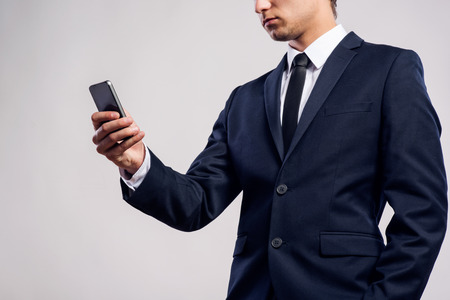 Close up of unrecognizable young hipster businessman with smartphone texting, reading, writing and searching something. Studio shot on gray background.の写真素材