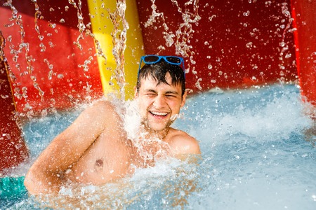 Man in swimmning trunks having fun under splashing fountain. Summer heat and water.の写真素材