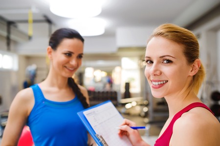 Close up, attractive fit woman in a gym consulting  work out with personal trainer, exercise plan on clipboardの写真素材