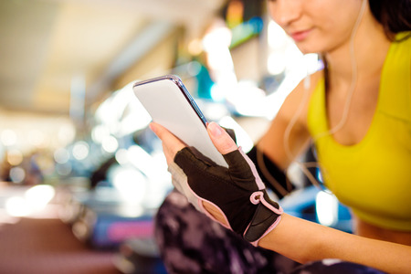 Attractive fit woman in a gym with smart phone against a row of treadmills