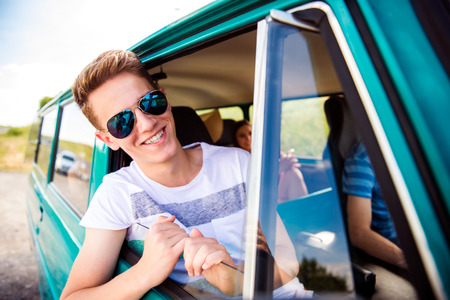 Teenagers inside an old campervan on a roadtrip, boy leaning out of window, sunny summer day