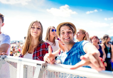 Teenagers at summer music festival under the stage in a crowd enjoying themselves, boy showing peace...