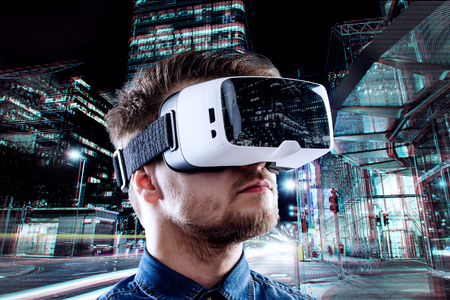 Man wearing virtual reality goggles against illuminated night city