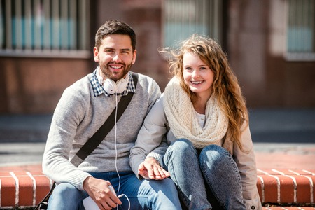 Young couple in love in town sitting on stairs, holding handsの写真素材