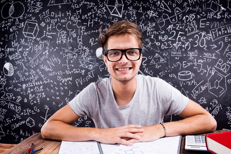 Hipster student with eyeglasses doing his homework in front of a big blackboardの写真素材