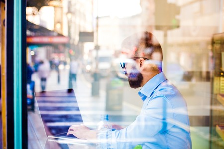 Hipster manager sitting in cafe by the window working on laptop, street reflectionの写真素材