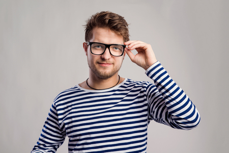 Hipster man in striped black and white long sleeve t-shirt and eyeglasses. Studio shot on gray backgroundの写真素材
