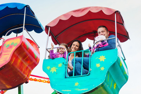 Cute little girls with their mother and father enjoying ride at fun fair, young family, amusement parkの写真素材