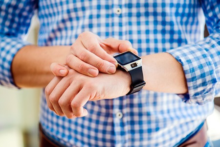 Close up of unrecognizable man in blue checked shirt using smart watchの写真素材